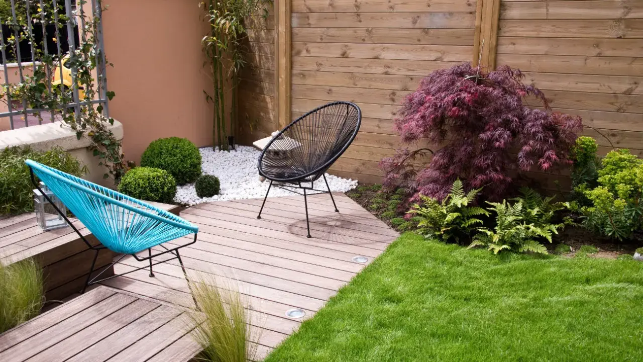 Aménagement d'un petit jardin de 100m2 : terrasse en bois, mobilier design, gazon et végétation luxuriante pour un espace détente moderne.