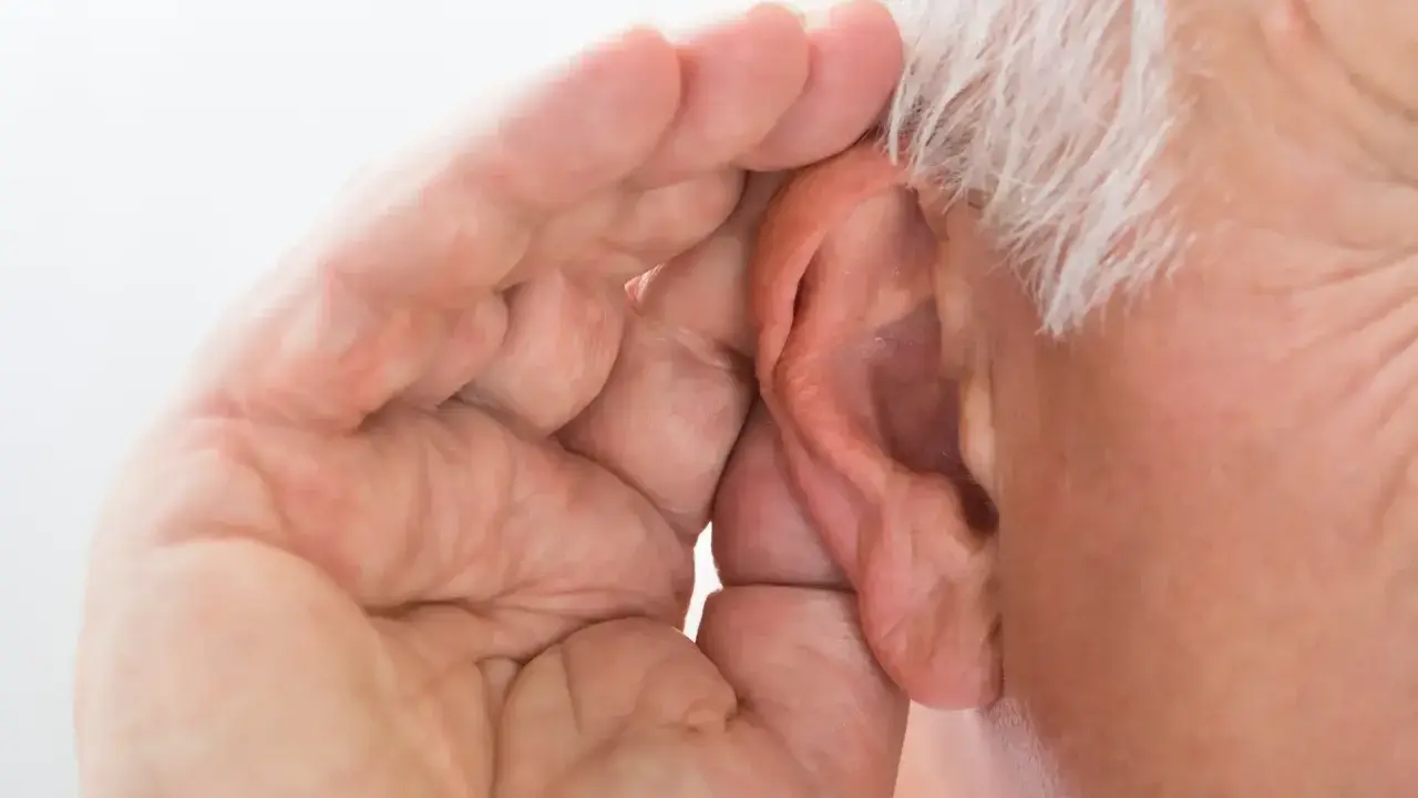 Mano di anziano che copre l'orecchio, forse per sentire meglio o per proteggersi da allucinazioni uditive.