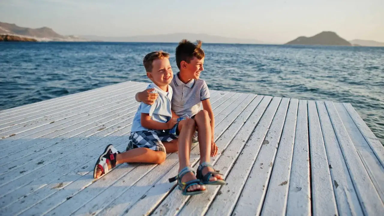 Dos niños sonríen sentados en un muelle blanco. ¡Ideas para que hacer en Murcia con niños!