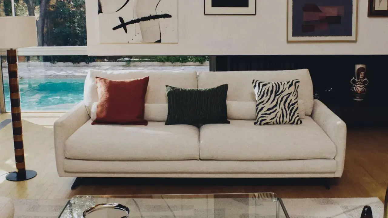 Sofá blanco con cojines decorativos: uno rojo, uno verde con textura y otro con estampado de cebra.