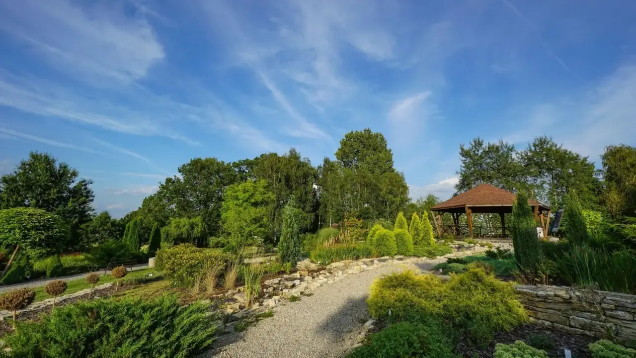 Malownicze ogrody botaniczne na Śląsku z altaną i kamiennymi ścieżkami, otoczone bujną zielenią pod błękitnym niebem.