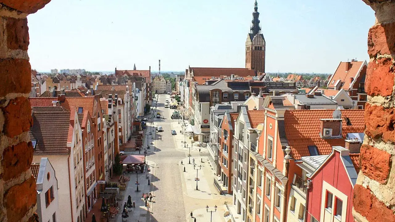 Widok z góry na urokliwą elbląg starówkę z kolorowymi kamieniczkami i wieżą kościelną w tle.