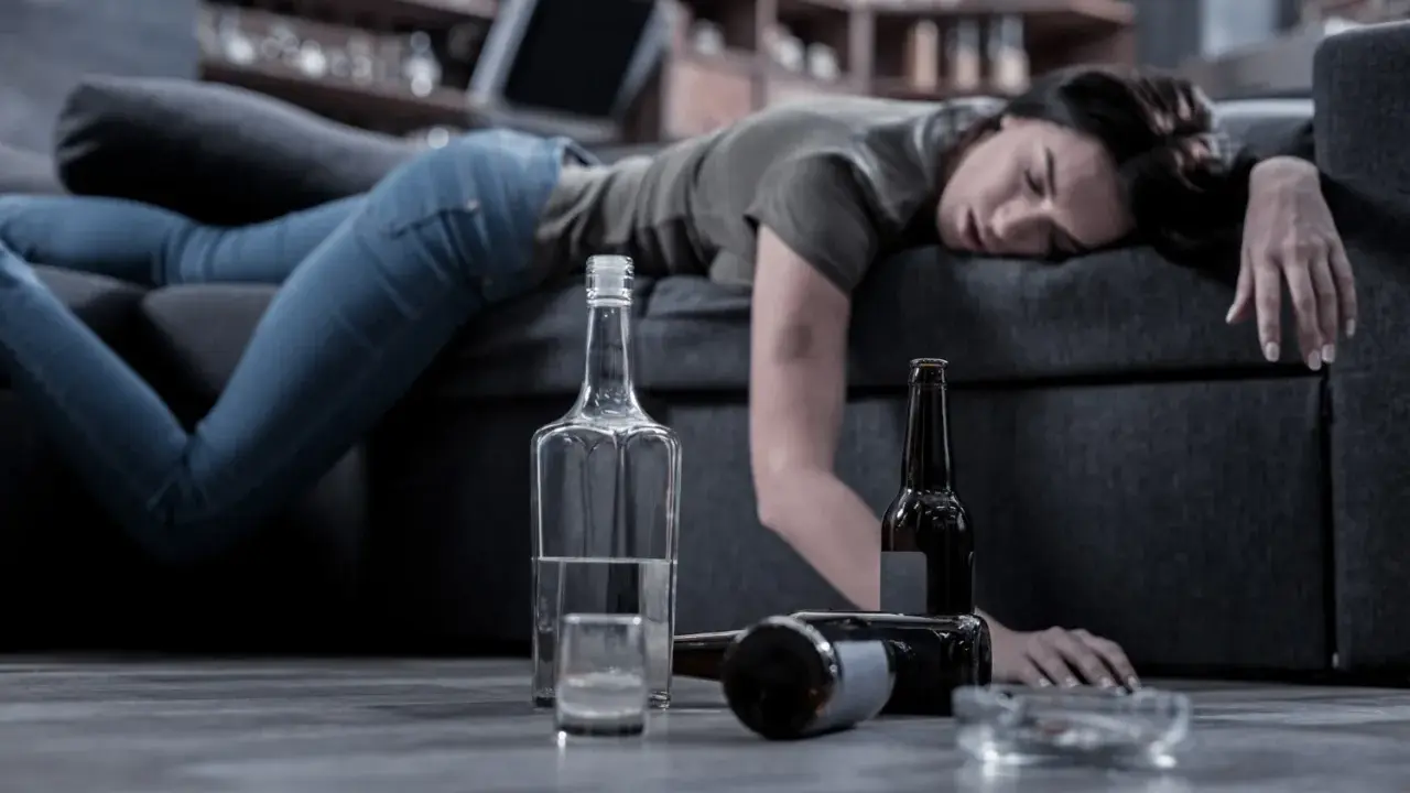 Kobieta leży nieprzytomna na kanapie, obok butelki i szklanka. Czy alkoholik może pić kontrolowanie? To pytanie pozostaje bez odpowiedzi.
