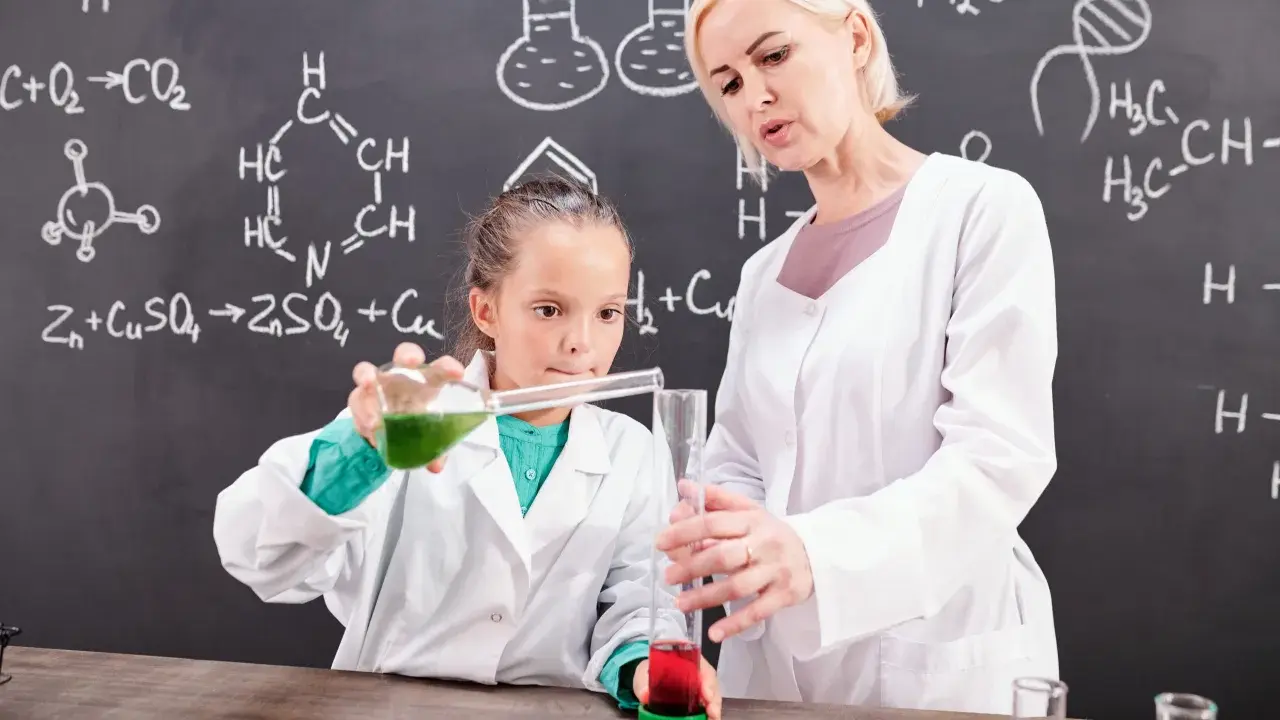 Nauczycielka chemii z pasją pokazuje uczennicy eksperyment. Ciekawe, ile zarabia nauczyciel chemii za taką pracę!