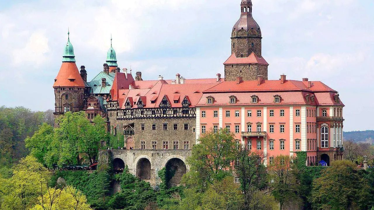 Malownicze zamki i pałace wokół Wrocławia, jak ten imponujący kompleks z wieżami i czerwonymi dachami, zachwycają architekturą i otoczeniem.
