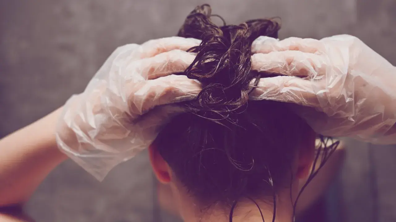 Hände mit Handschuhen tragen Olaplex Nr. 3 auf nasses, dunkles Haar auf.