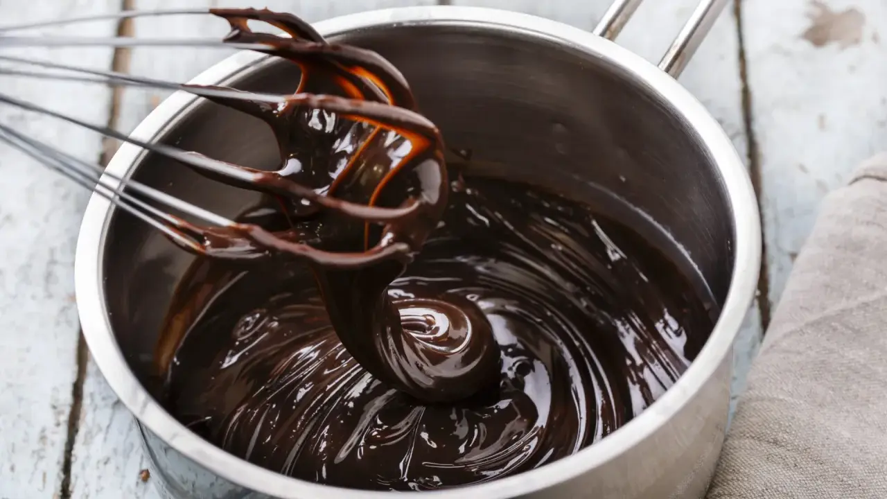Fouet mélangeant du chocolat noir brillant dans une casserole, étape clé pour le tempérage.
