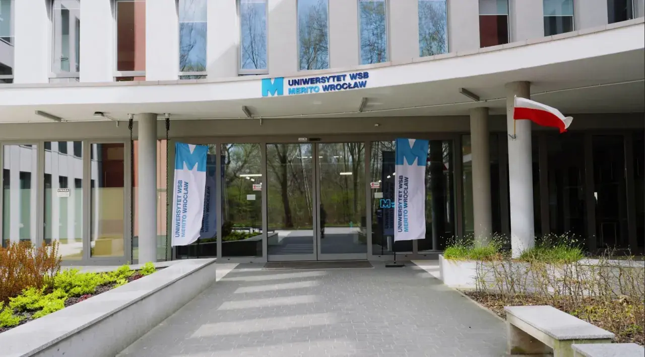 Wejście do Uniwersytetu WSB Merito Wrocław. Flagi z logo uczelni i polska flaga. Idealne miejsce na studia anglistyka Wrocław.