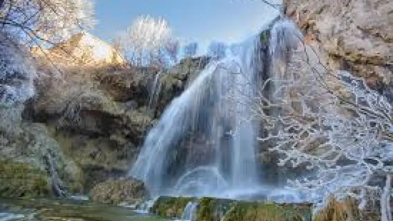 Cascada helada en el nacimiento del río Júcar, con ramas cubiertas de escarcha y agua cayendo sobre rocas.