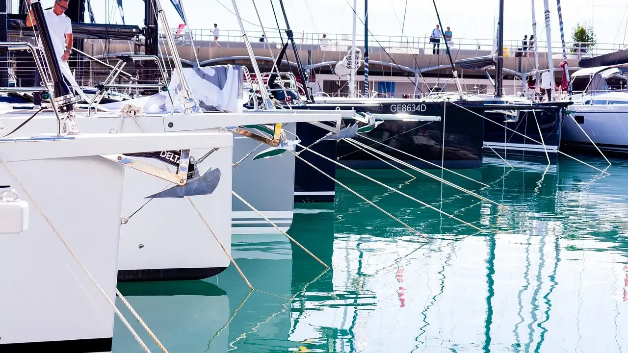 Des voiliers modernes, prêts à prendre la mer, sont amarrés dans un port. Leurs proues blanches et leurs ancres visibles rappellent le cale bateau.