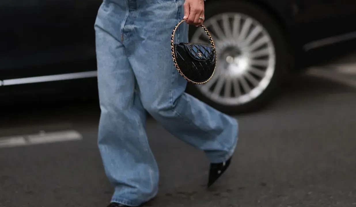 Spodnie baggy damskie stylizacje: luźne jeansy, biały sweterek i czarna torebka z łańcuszkiem.