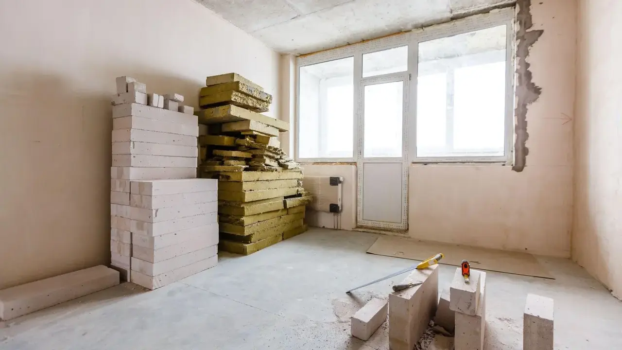 Materiały budowlane: pustaki i wełna mineralna, gotowe do ocieplenia od wewnątrz. Narzędzia budowlane leżą na podłodze.