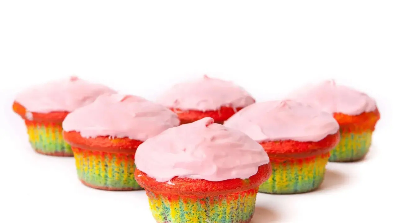 Bunte Muffins mit Lebensmittelfarbe und rosa Zuckerguss, die wie ein Regenbogen aussehen.