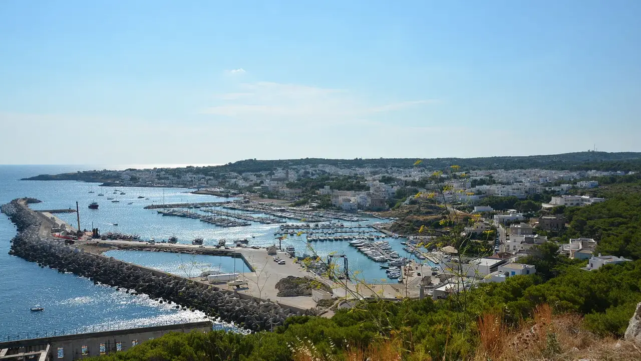 Vista panoramica del porto turistico di Santa Maria di Leuca, in provincia di Lecce, con numerose barche ormeggiate e la città bianca sullo sfondo.