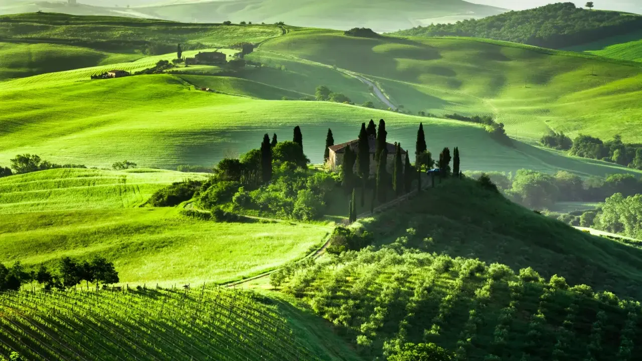 Colline verdi ondulate in Toscana, con una villa su una collina circondata da cipressi. Un sogno per un viaggio in Toscana.