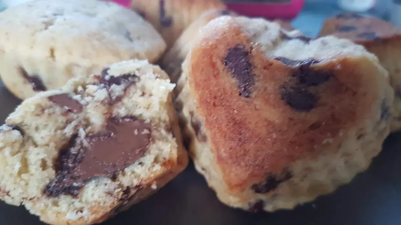Gros plan sur des cookies moelleux en forme de cœur, débordant de pépites de chocolat. Un cookie est coupé en deux, révélant un cœur fondant.