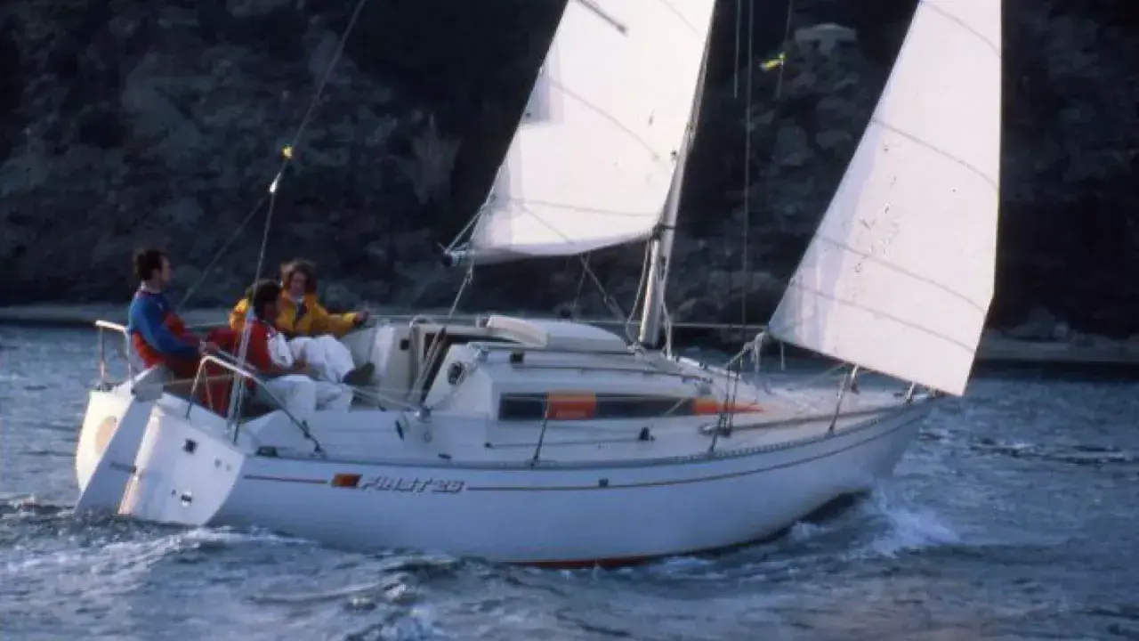 Trois personnes naviguent sur un voilier blanc, le "Pirat 26". Les voiles sont gonflées par le vent, créant une scène paisible.