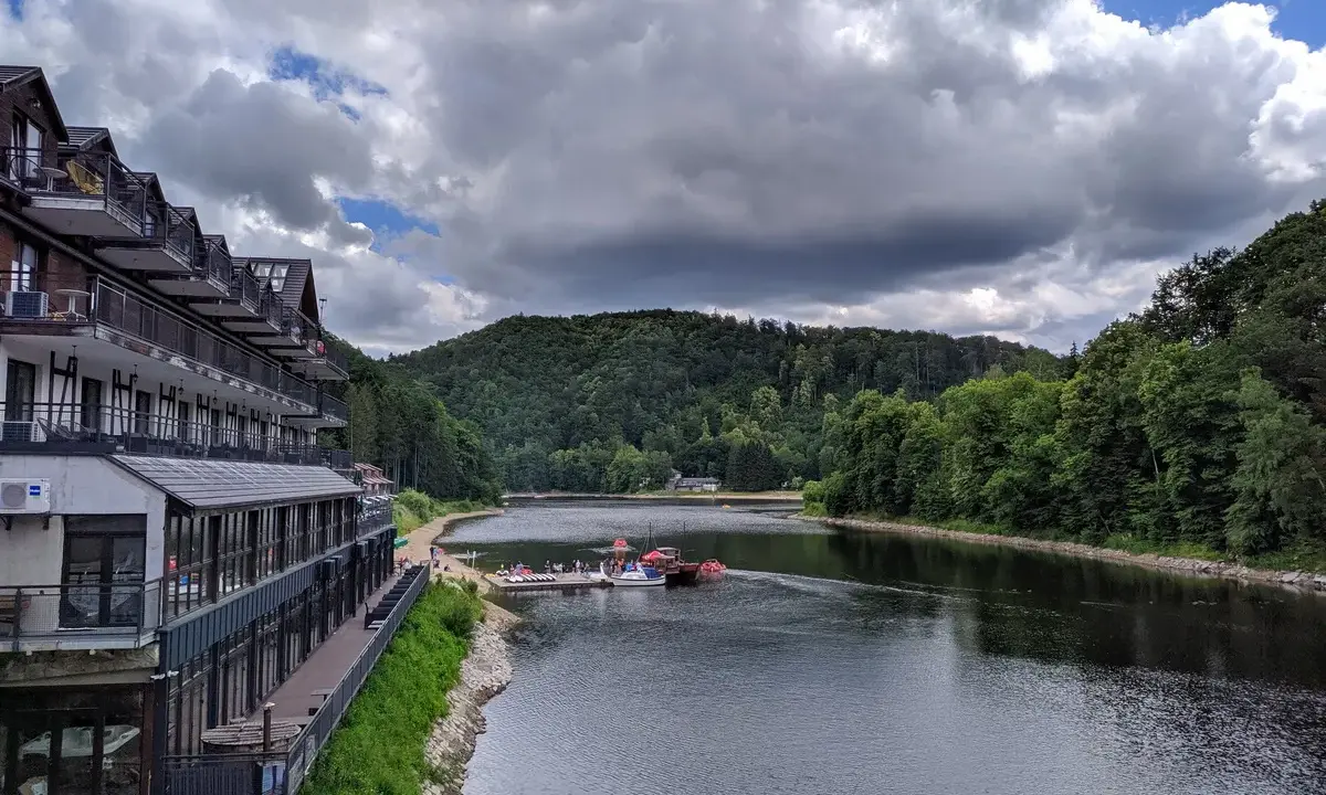 Hotel nad jeziorem Bystrzyckim, z plażą i pomostem, gdzie cumują łódki.