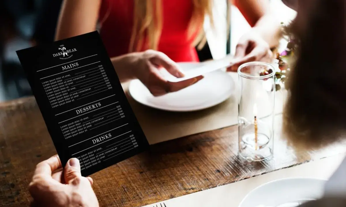 Mężczyzna trzyma czarne menu restauracji "The Dark Bear". Co to jest laminat? To trwałe menu, idealne do restauracji.