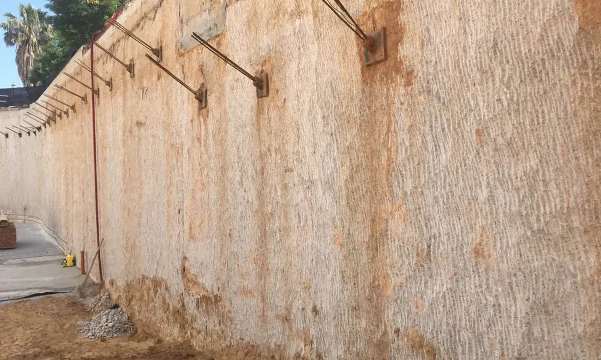 Muros pantalla de contención con anclajes metálicos, mostrando la textura rugosa de la roca y la tierra.