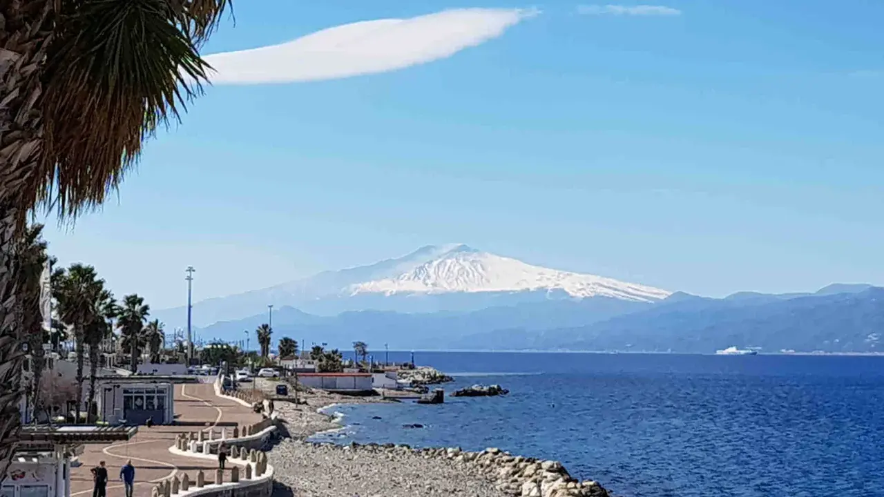 Lungomare di Reggio Calabria con vista sull'Etna innevato. Perfetto per scoprire cosa visitare a Reggio Calabria, tra palme e mare blu.