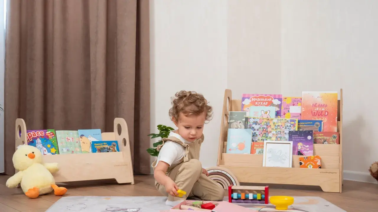 Kleines Kind spielt mit Holzspielzeug vor einem Regal mit Büchern, das eine Sitzordnung im Montessori-Stil widerspiegelt.