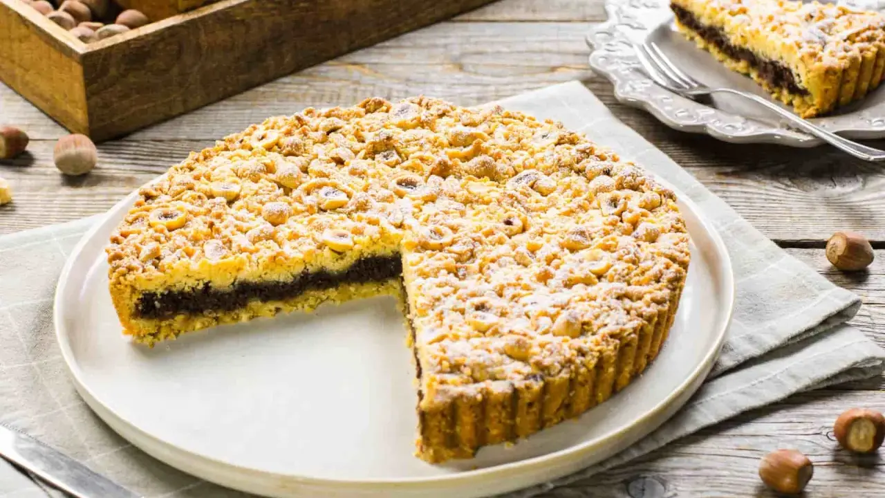 Sbriciolata alla Nutella con tante nocciole croccanti, un dolce invitante su un piatto bianco, pronto per essere gustato.