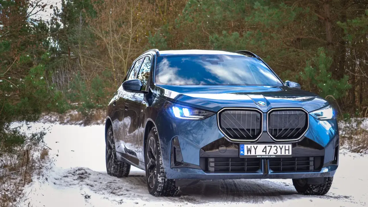 Niebieskie, nowe BMW X3 na ośnieżonej drodze w lesie. Zimowe opony gotowe na wyzwania.