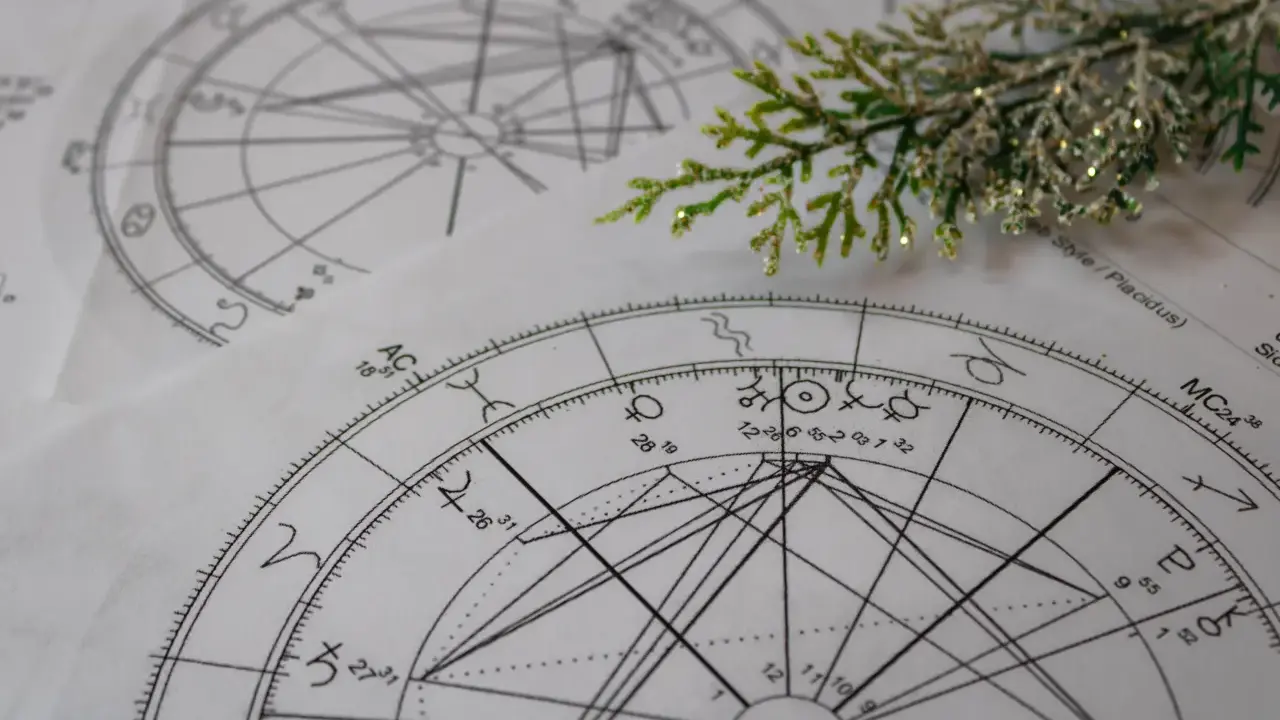 Zrozumienie, jak czytać kosmogram, to klucz do odkrywania tajemnic wszechświata. Na zdjęciu widać fragmenty kosmogramów, symboli astrologicznych i gałązkę iglastą.