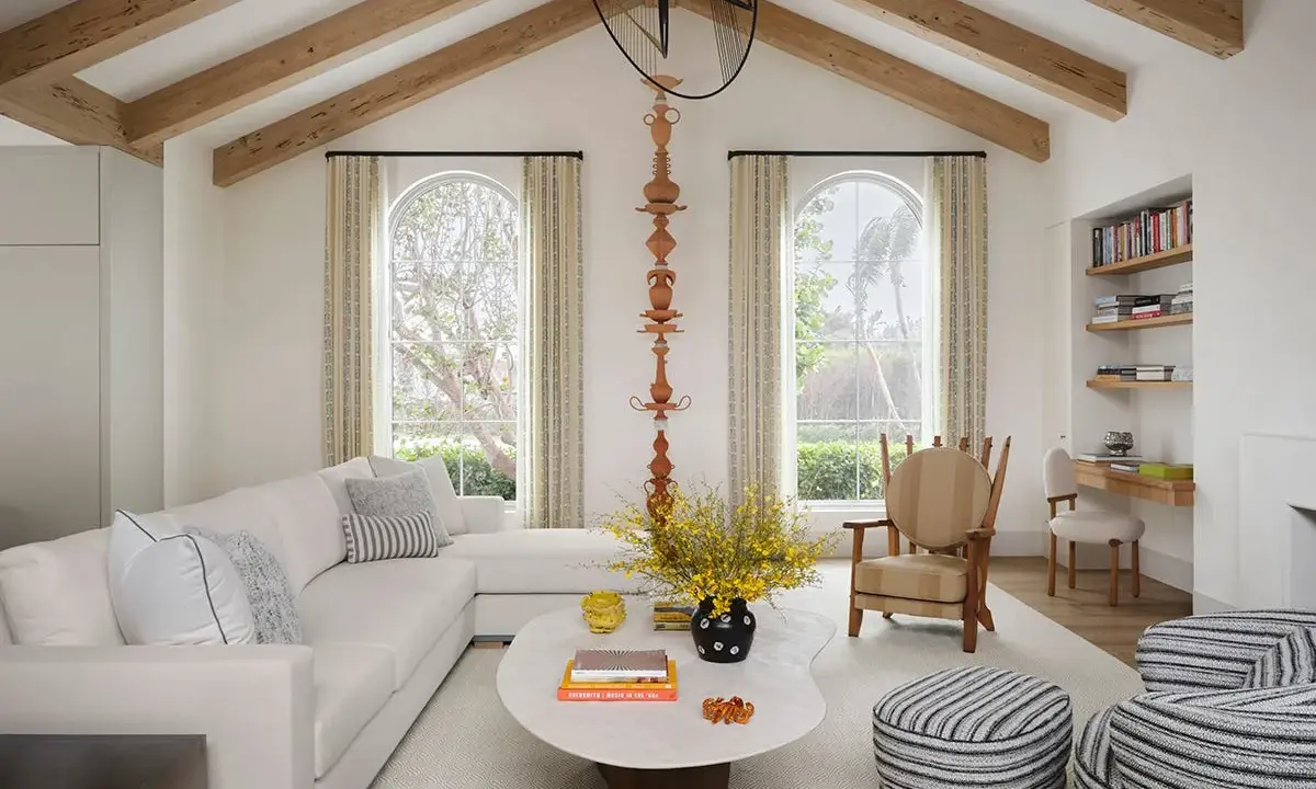 Salón luminoso con vigas de madera en el techo, creando la sensación de casas con techos bajos. Sofá blanco, mesa ovalada y butaca a rayas.