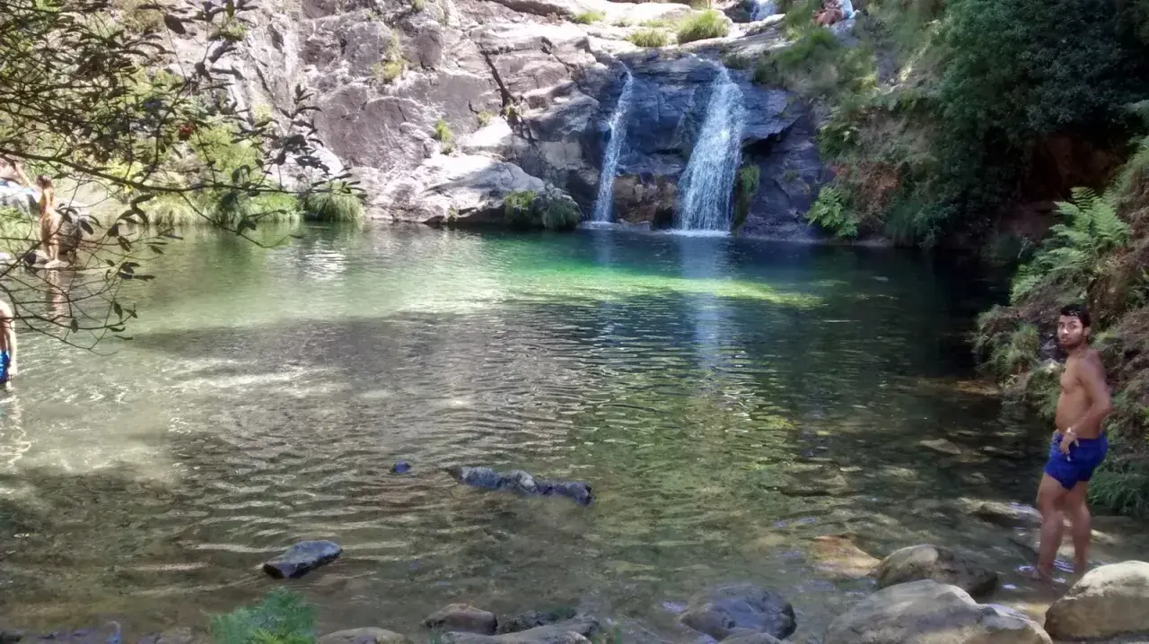 Un hombre disfruta de las pozas de Mougas, con cascadas cayendo sobre rocas y vegetación exuberante.