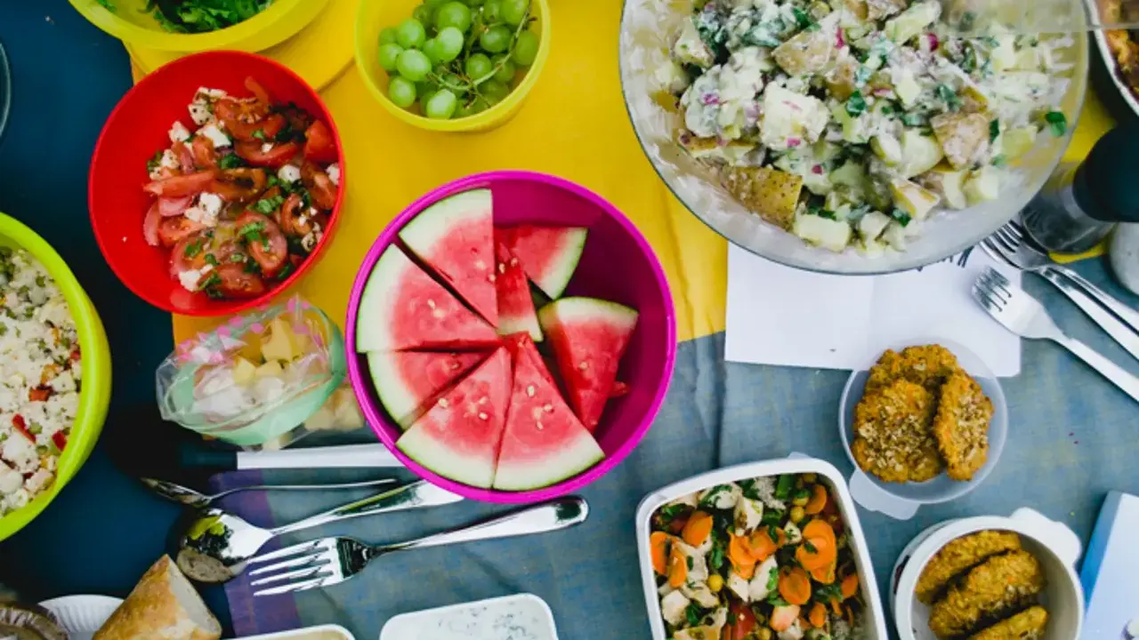 Bunte Schüssel mit Wassermelone, Kartoffelsalat, Trauben und Tomatensalat – leckere Picknick-Snacks für einen sonnigen Tag.