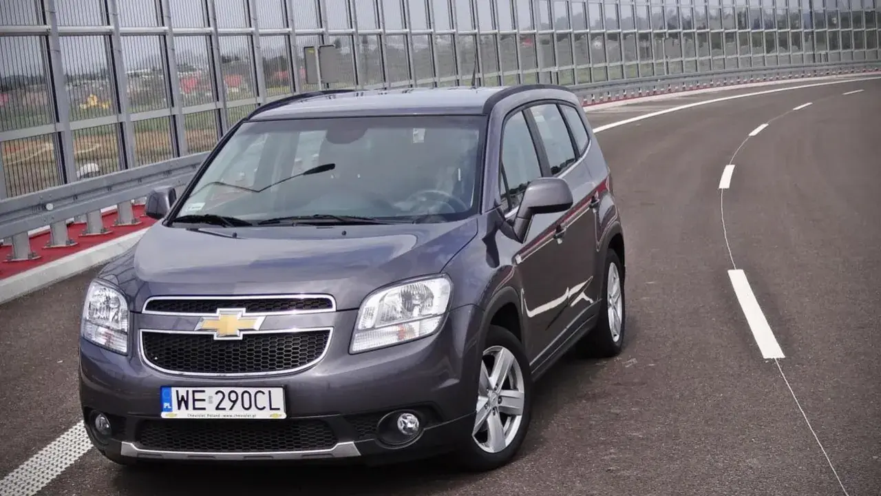 Szary Chevrolet Orlando 1.8 benzyna na pustej drodze, za barierami dźwiękochłonnymi.