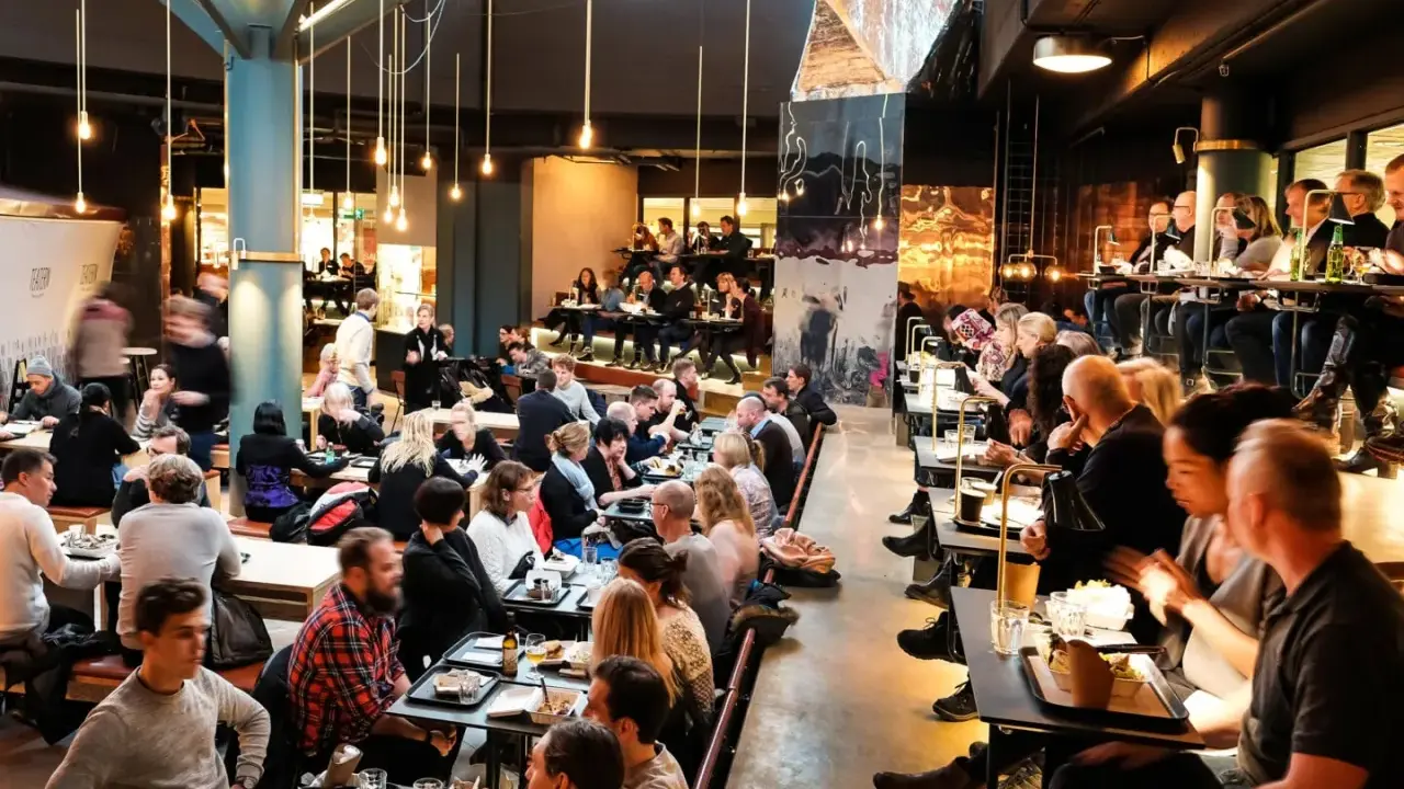 Folk äter och umgås på en livlig **Ringen food court**. Många bord är upptagna, stämningen är social och maten ser god ut.