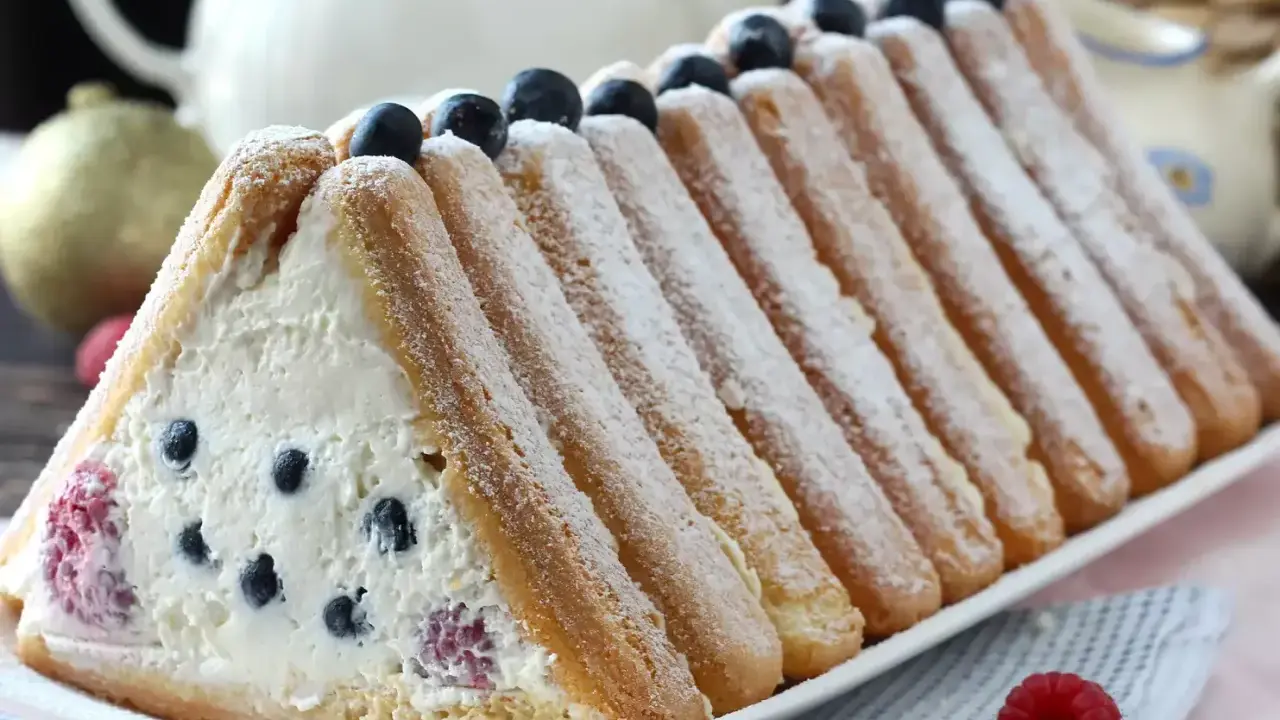 Délicieuse recette buche fruits rouges : un gâteau léger garni de crème et de baies, entouré de biscuits à la cuillère saupoudrés de sucre glace.