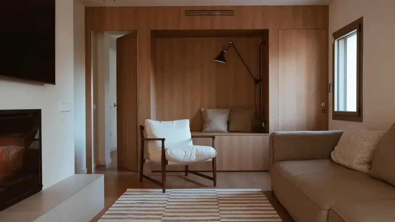 Salones pequeños con mueble de madera integrado, sofá, sillón blanco y alfombra a rayas.