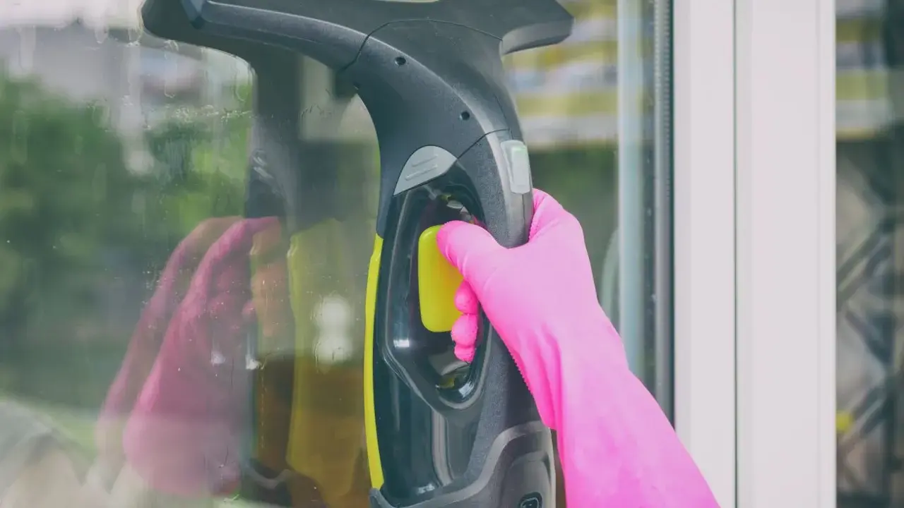 Ręka w różowej rękawiczce trzyma myjkę do okien Kärcher, czyszcząc szybę.