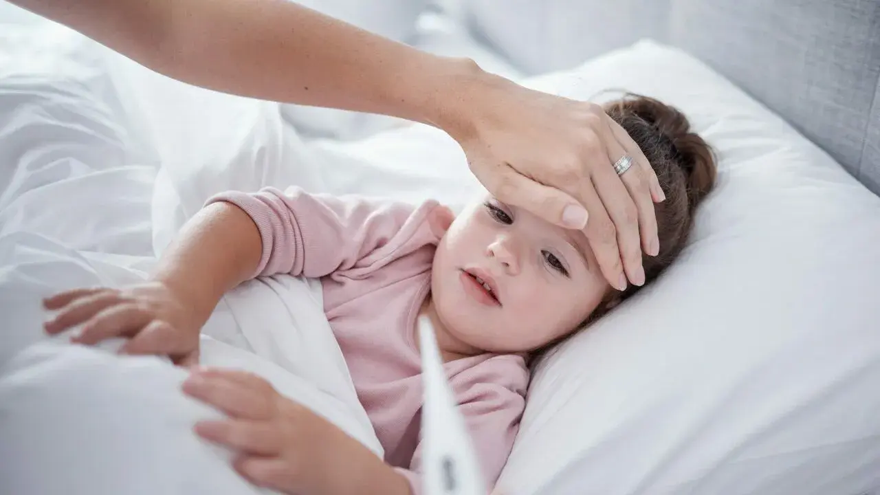 Mama sprawdza temperaturę chorego dziecka, martwiąc się przegrzaniem.