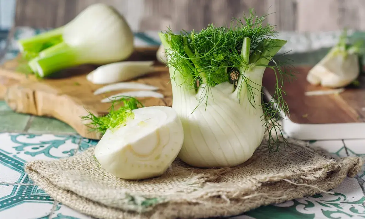 Fenouil frais, prêt à révéler ses bienfaits. Une moitié coupée montre sa texture croquante, tandis que le bulbe entier déploie ses feuilles aériennes.
