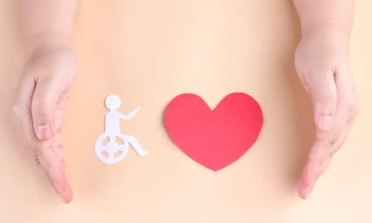 Dwie dłonie obejmują symbol osoby na wózku i serce. Symbolizuje to troskę o osoby z znacznym stopniem niepełnosprawności a alimenty.