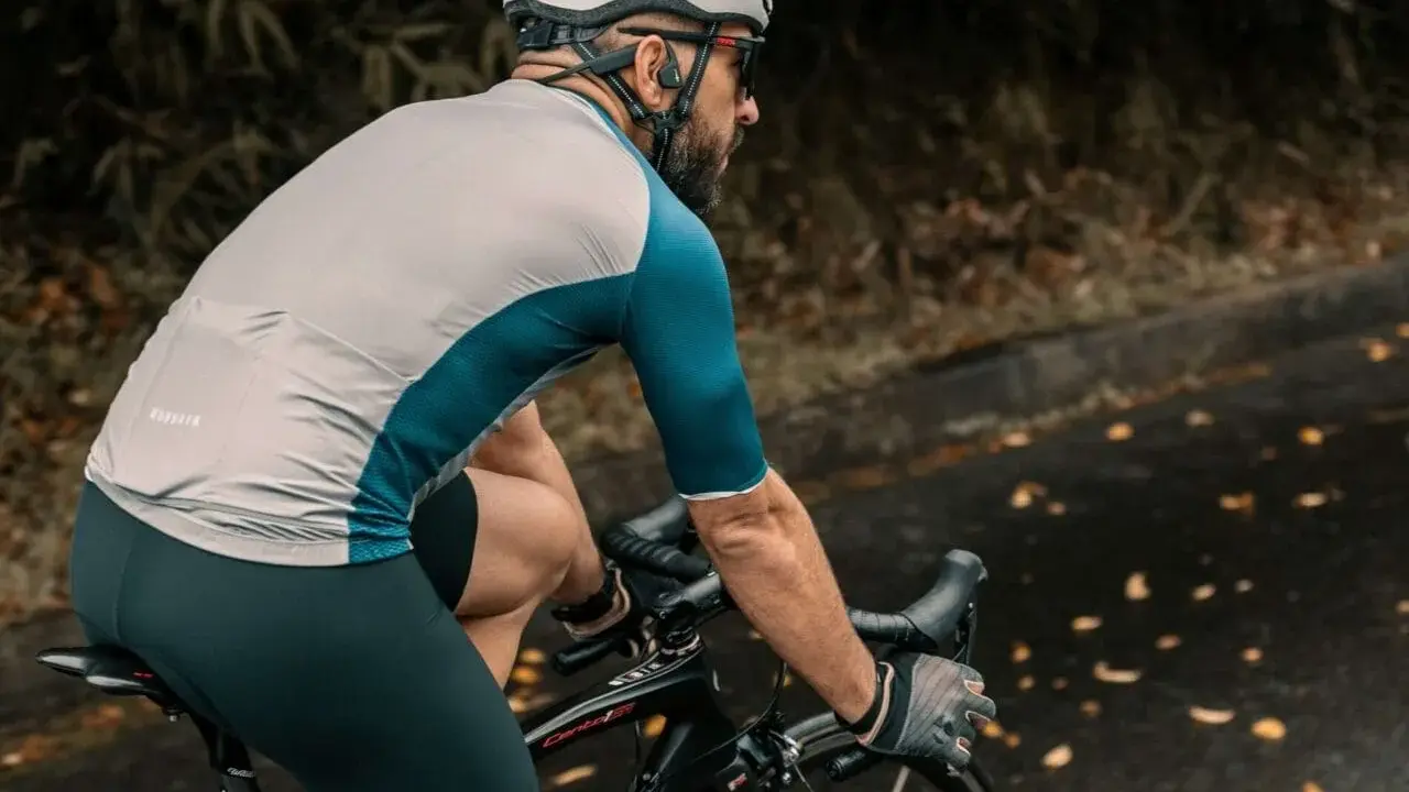 Ciclista con casco e occhiali pedala su strada bagnata, godendosi l'aria fresca. Un modo perfetto per alternare bici e camminata.
