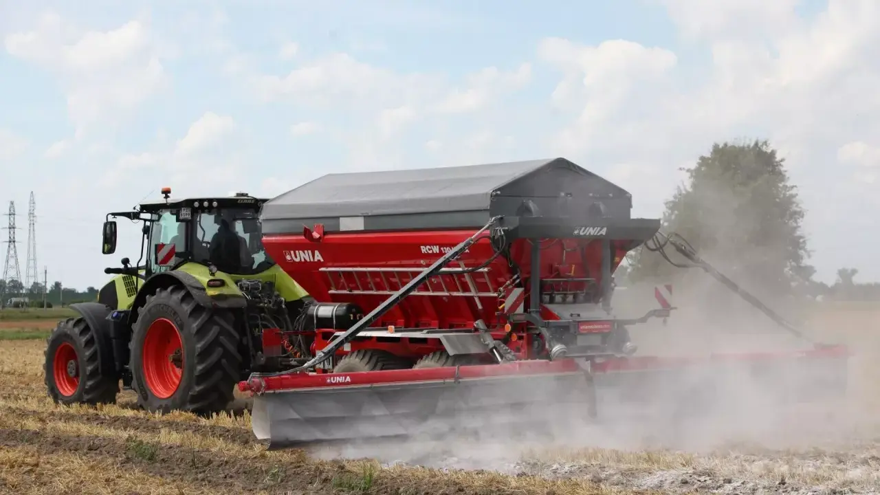 Traktor z rozsiewaczem wapna RCW 1300 marki UNIA na polu. To idealne rozwiązanie, jakie wapno pod warzywa, by zapewnić im najlepsze warunki do wzrostu.