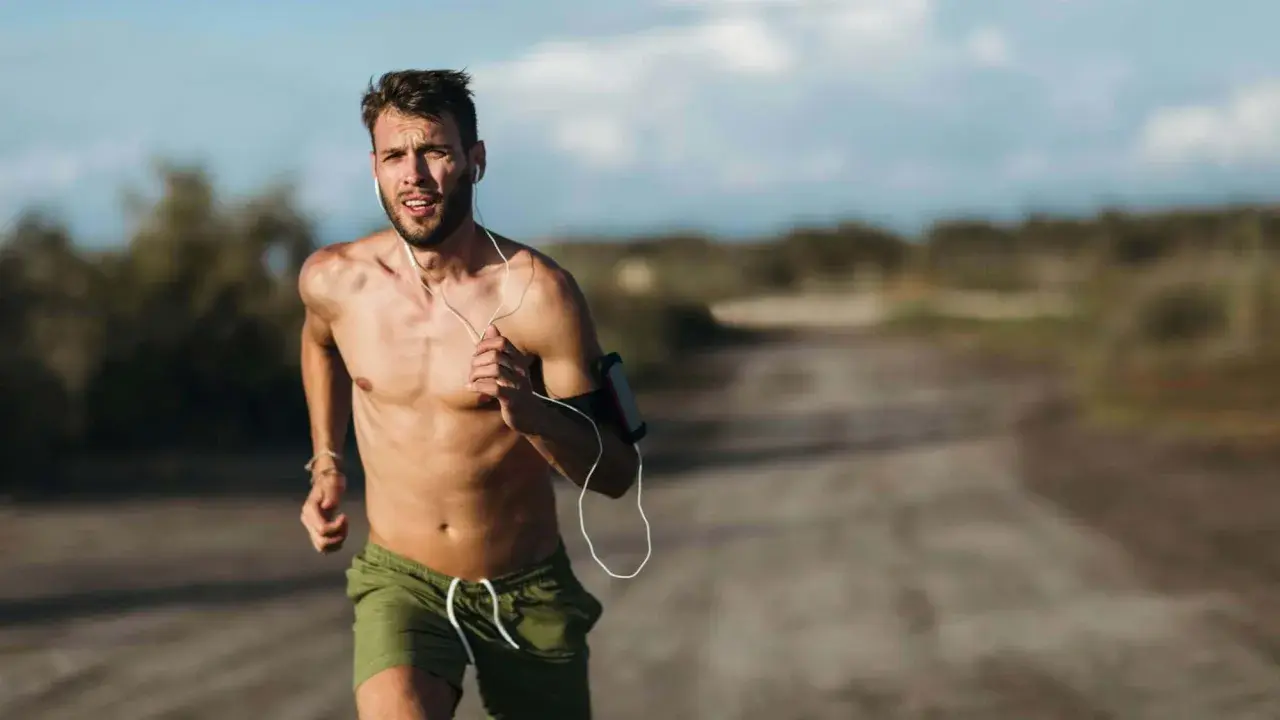 Ein Mann läuft bei Hitze, sein Puls rast. Er trägt Kopfhörer und eine Armbinde für sein Handy.
