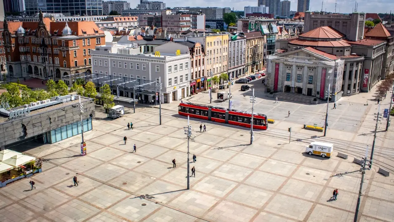 Rynek w Katowicach z czerwonym tramwajem i ludźmi spacerującymi po placu. Idealne miejsce na odkrywanie katowickich atrakcji dla młodzieży.