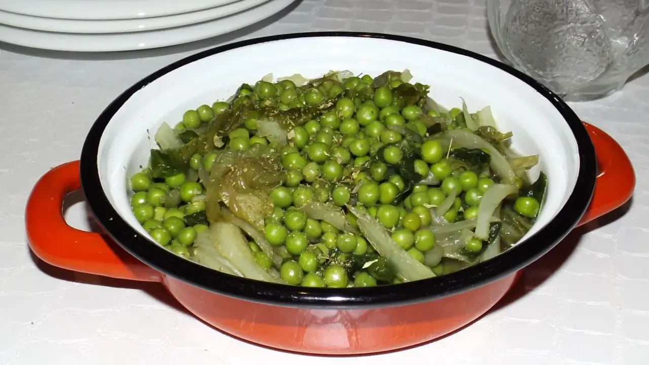Un plat de petits pois et légumes verts, assaisonnés d'herbes, dans une cocotte orange. Une recette simple et savoureuse.