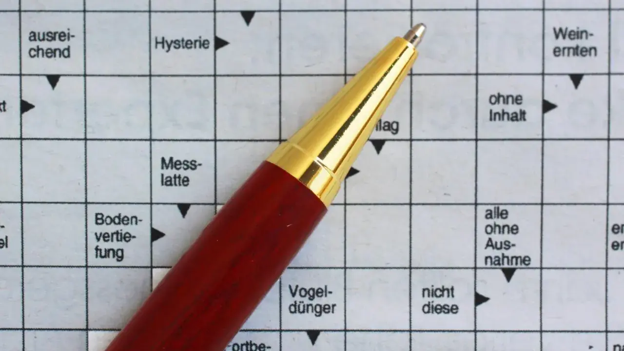 Ein roter Stift liegt auf einem Kreuzworträtsel mit deutschen Begriffen.