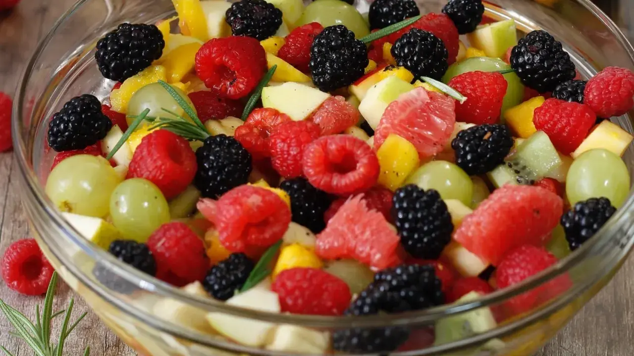 Un bol de salade de fruits frais et colorée, garnie de framboises, mûres, raisins verts, morceaux de pomme, pamplemousse et kiwi.