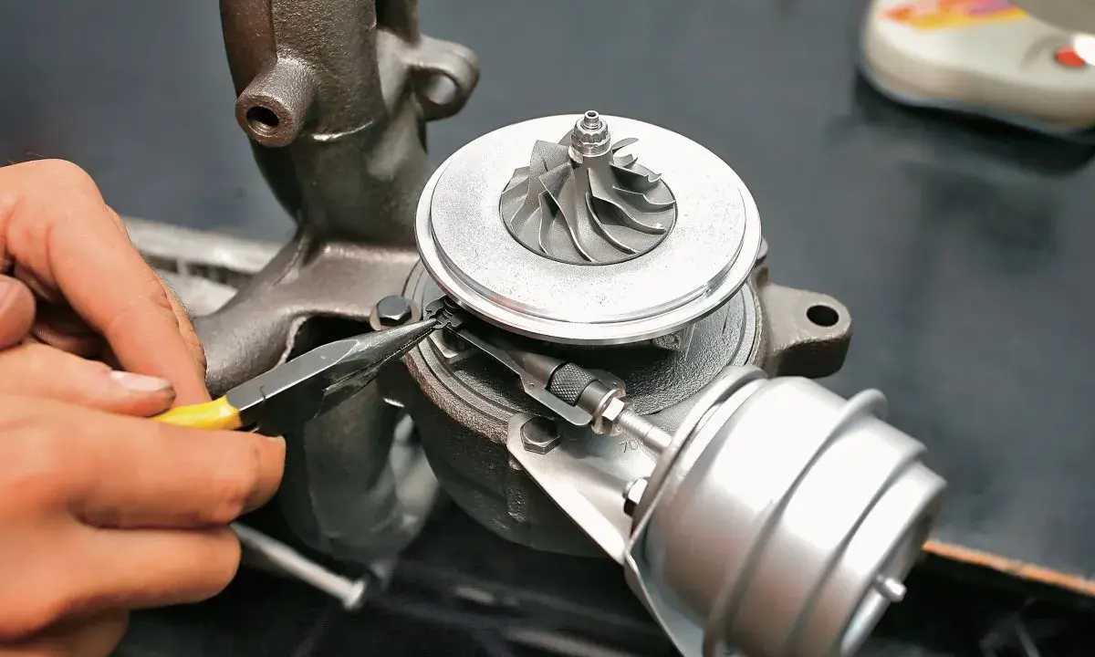 Dłoń z kombinerkami reguluje mechanizm turbosprężarki, precyzyjnie ustawiając geometrię turbiny.