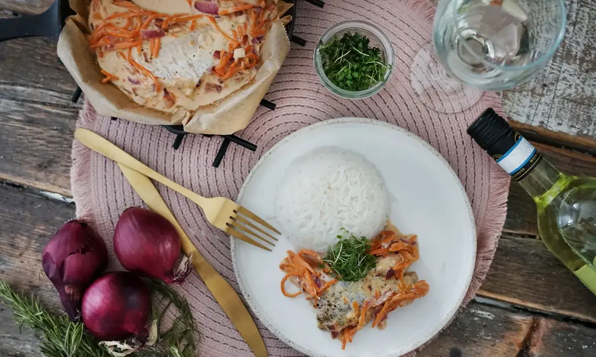 Ein Rotbarschfilet mit Senfsauce, serviert mit Reis und garniert mit Kresse. Dazu passen rote Zwiebeln und ein Glas Weißwein.