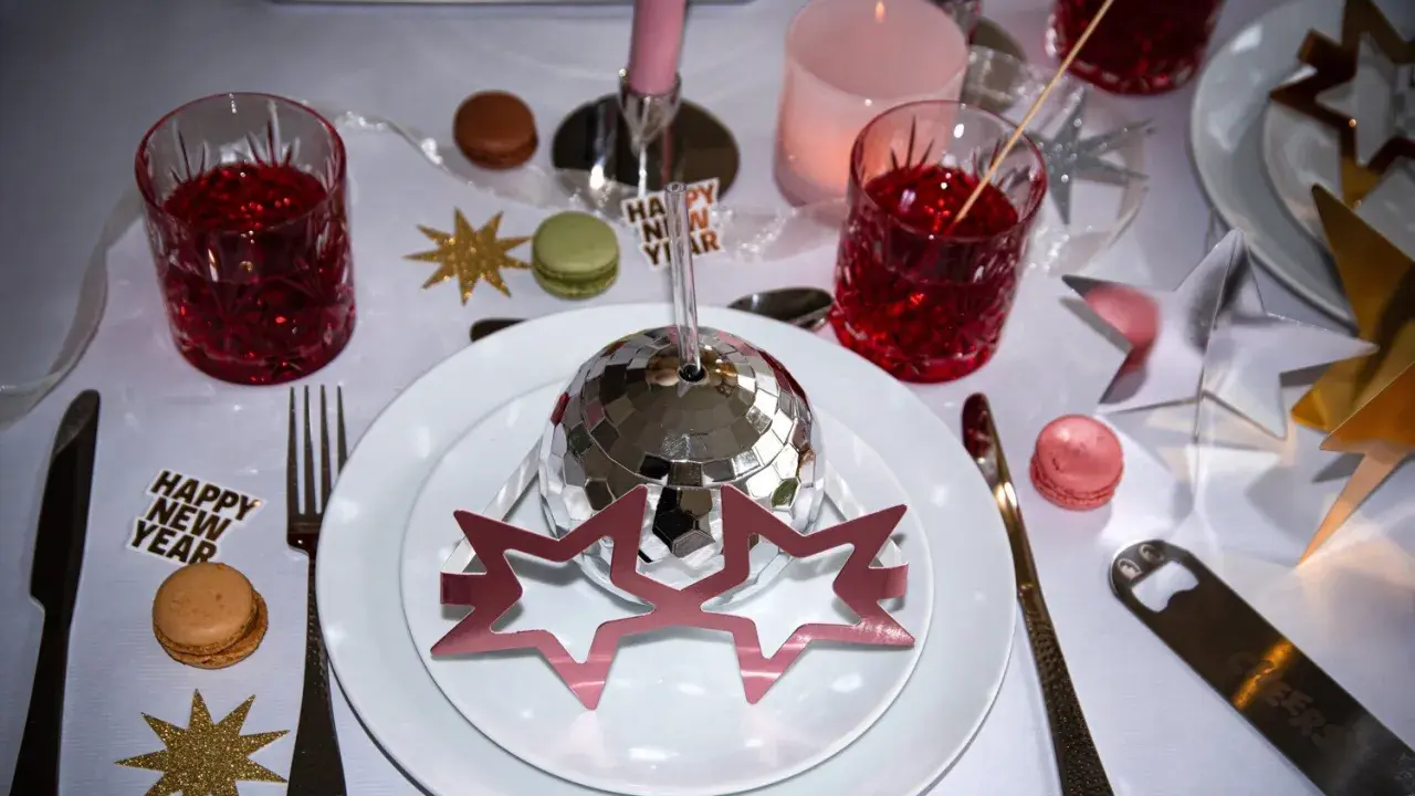 Enkel nyårsdukning med disco-boll, stjärnor, macarons och röda drinkar. En festlig och glittrig bordsdekoration för att fira in det nya året.
